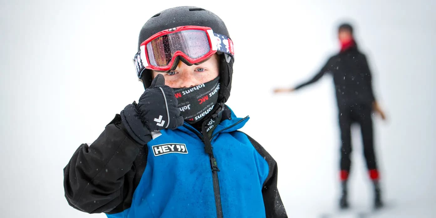 En ung pojke i blå overall som åker skidor.