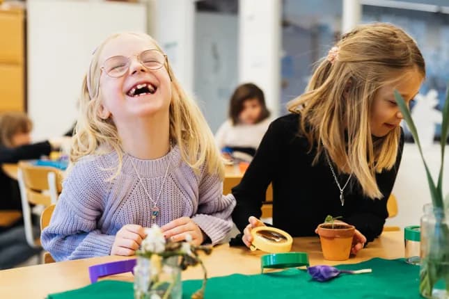 Två unga flickor sitter vid ett bord i ett klassrum.