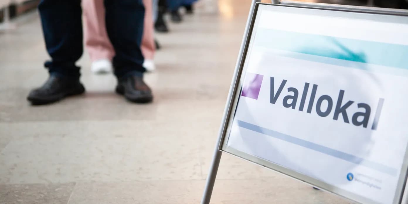 En skylt som säger vallokal framför en grupp människor.