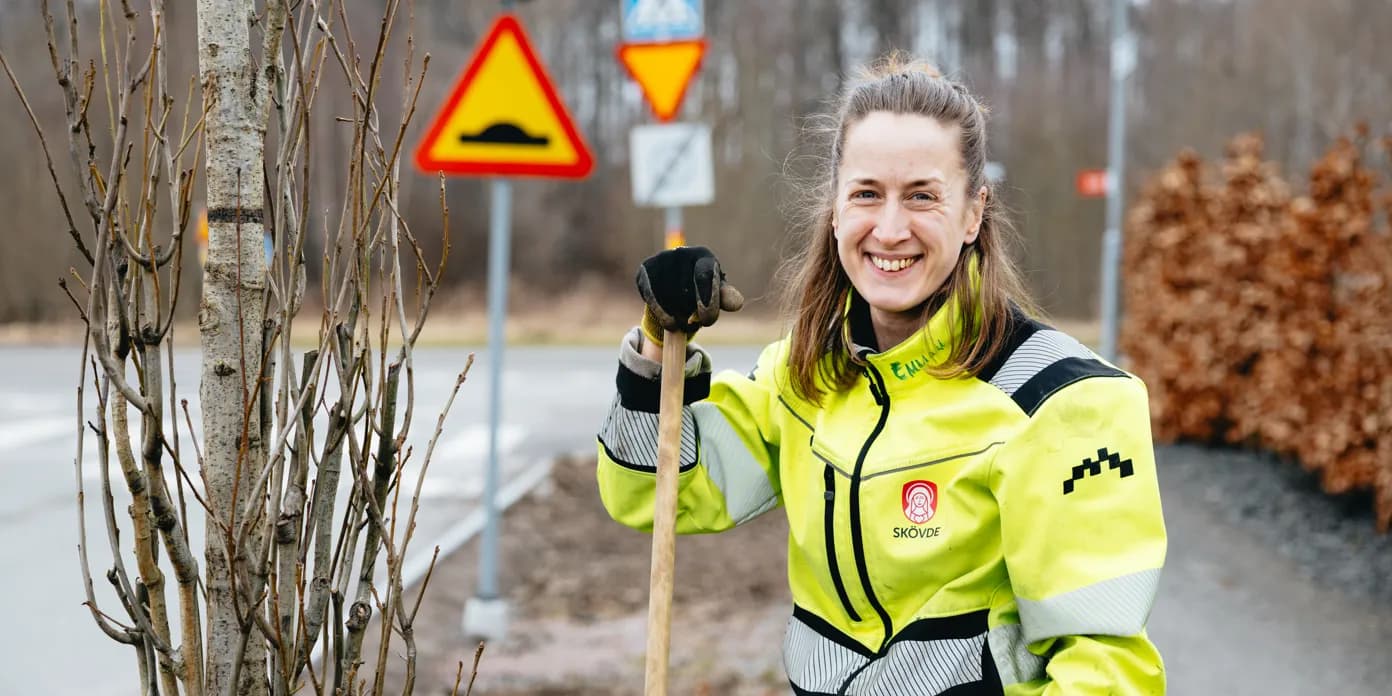 En kvinna håller i en spade bredvid ett träd