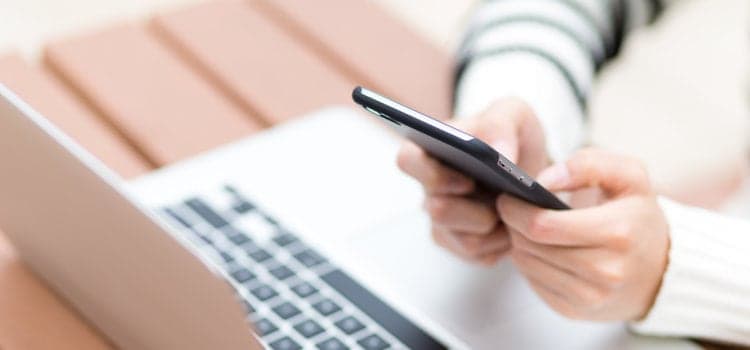En person som använder en mobiltelefon medan han sitter framför en bärbar dator